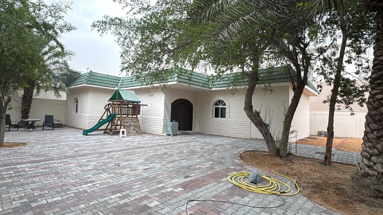 Freshly repainted single-storey villa with green tiled roof trim, new interlock paving and garden play area after exterior renovation in Al Quoz, Dubai