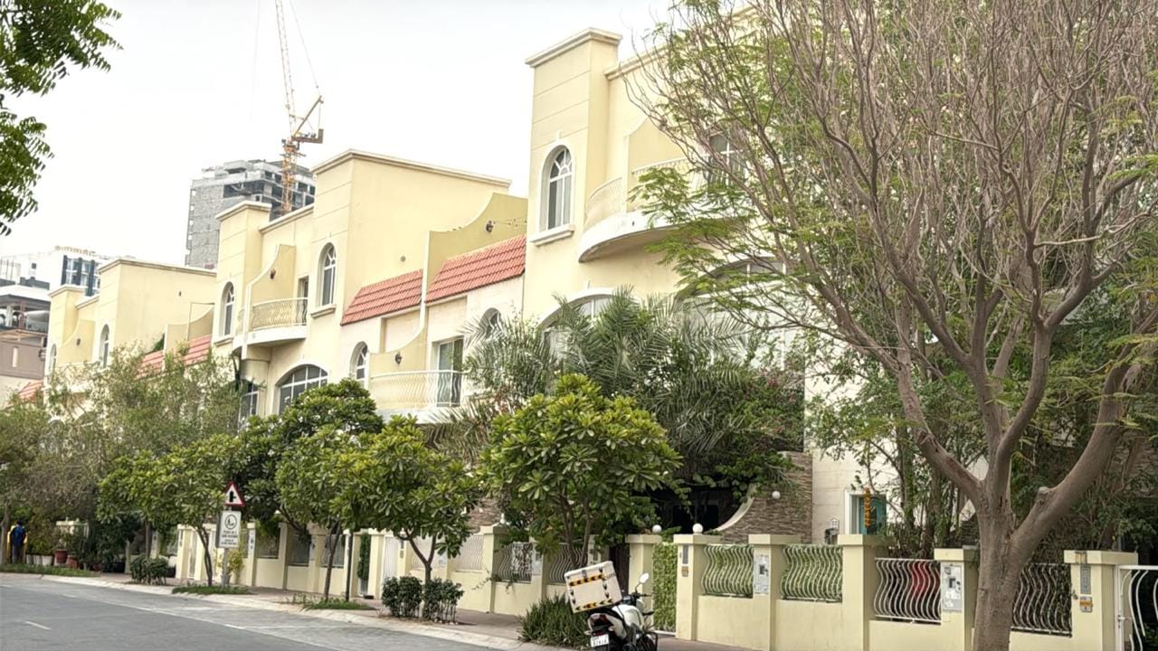 Tree-lined JVC street of townhouses with Dubai high-rises under construction behind