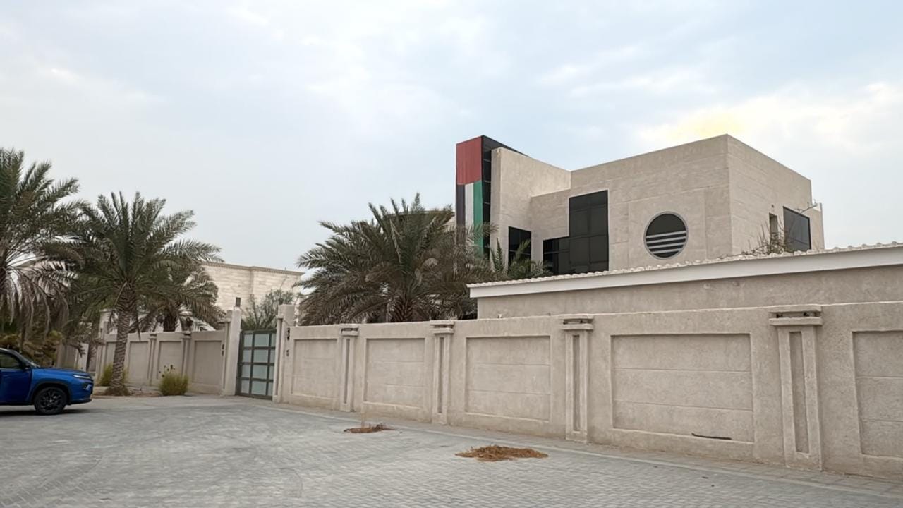 Stone boundary wall and gate to a modern Nad Al Sheba villa, with a circular louvred window in the upper stone mass behind