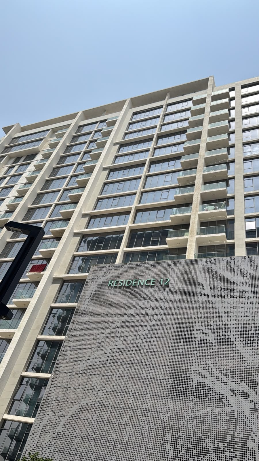 Residence 12 seen from a second angle, with green signage set on the perforated screen and rows of projecting balconies on the storeys above